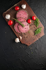 Smoked salami on a black table and a brown board. Sausages with rosemary, garlic and pepper and tomato cherry, dill, parsley.