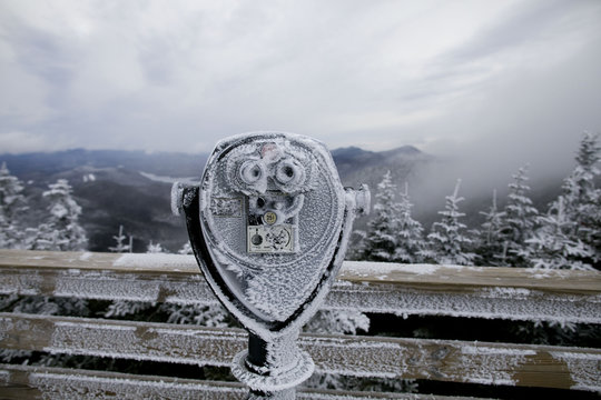 Frozen coin operated binoculars at observation point against mountains