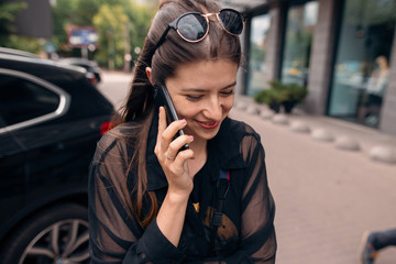 beautiful hipster girl holding phone and talking in city street. stylish happy woman having conversation by smartphone and smiling. space for text