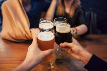 hands of people holding beer and cheering in brewery pub. people toasting with delicious beer  in bar. friends drinking and enjoying a beer. leisure and friendship  concept