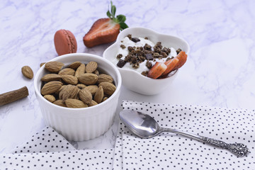 Stylishly decorated and healthy breakfast - strawberries, yoghurt with granola and almonds on a white marble background.