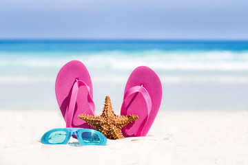 Fototapeta na wymiar Pink flip flops, swimming glasses and starfish on white sandy beach