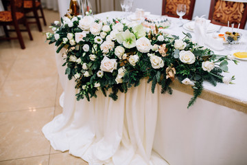 wedding table of the newlyweds with a composition of roses, eustoma of white color, spruce, a pistachio covered with a white cloth