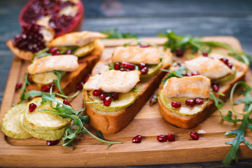 Tasty crunchy italian snack bruschetta with grilled chicken, zucchini, pomegranate seeds and arugula on wooden board
