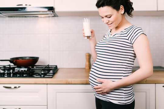 Close up details of attractive brunette pregnant wife drinking milk in white kitchen