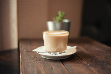 Delicious cappuccino and saucer are on a wooden table in the cafe