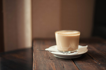 Delicious cappuccino and saucer are on a wooden table in the cafe