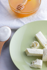 Cheese, honey and sour cream, feta in green plate, soft cheese on white background, wooden spoon with sour cream, French breakfast, blue napkin, honey in glass dishes, art