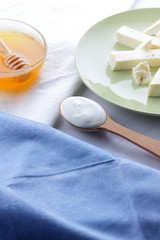 Cheese, honey and sour cream, feta in green plate, soft cheese on white background, wooden spoon with sour cream, French breakfast, blue napkin, honey in glass dishes, art