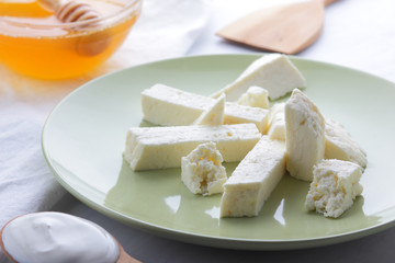 Cheese, honey and sour cream, feta in green plate, soft cheese on white background, wooden spoon with sour cream, French breakfast, blue napkin, honey in glass dishes, art