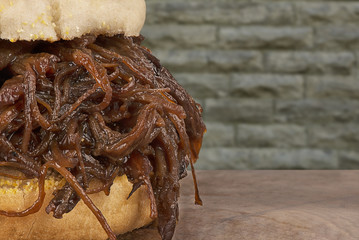 Close up on pulled pork sandwich, wall of brick in background.