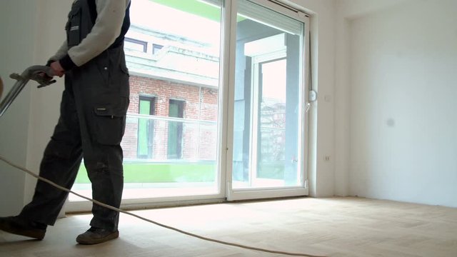 Sanding hardwood floor with the grinding machine. Repair in the apartment. Carpenter doing parquet wood floor polishing maintenance work by grinding machine