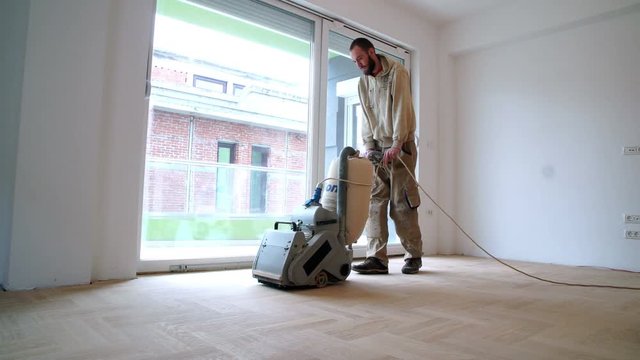 Sanding hardwood floor with the grinding machine. Repair in the apartment. Carpenter doing parquet wood floor polishing maintenance work by grinding machine