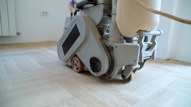 Sanding hardwood floor with the grinding machine. Repair in the apartment. Carpenter doing parquet wood floor polishing maintenance work by grinding machine