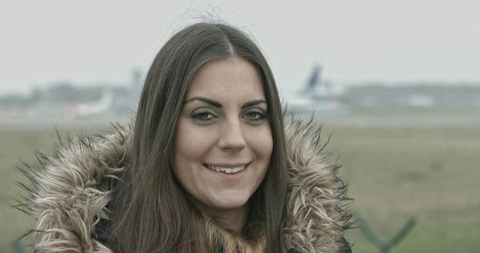 Woman looking at camera and smiling. Airport in background.