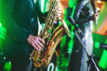 Concert view of a saxophone player with vocalist and musical jazz band in the background