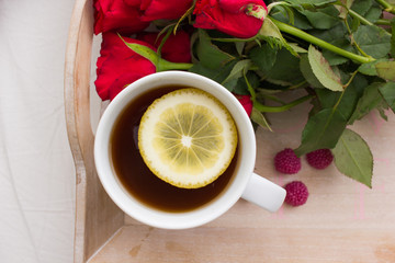 White cup of the black tea with lemon and red roses