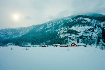 Astonishing outdoor view of traditional Norwegian red houses of wood covered with snow in the roof in stunning nature background in Norway