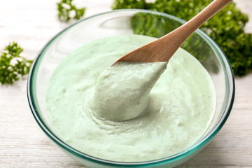 Spoon with tasty creamy sauce for fish taco in bowl on table