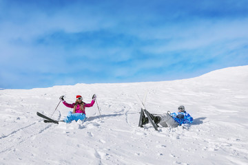 Fallen couple on ski piste at snowy resort. Winter vacation