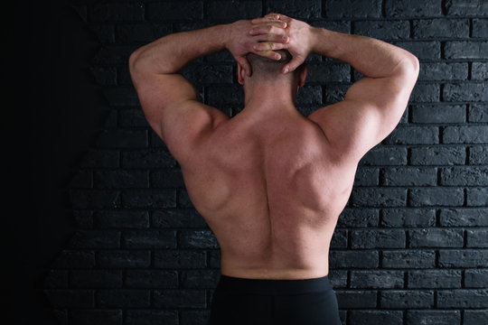 young strong bodybuilder posing near the old brick wall. part of body: the broad back and muscular male ass. bald head guy in tights. athletic figure after exercise and diet