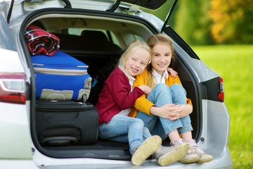 Two adorable little girls sitting in a car before going on vacations with their parents. Two kids looking forward for a road trip or travel.