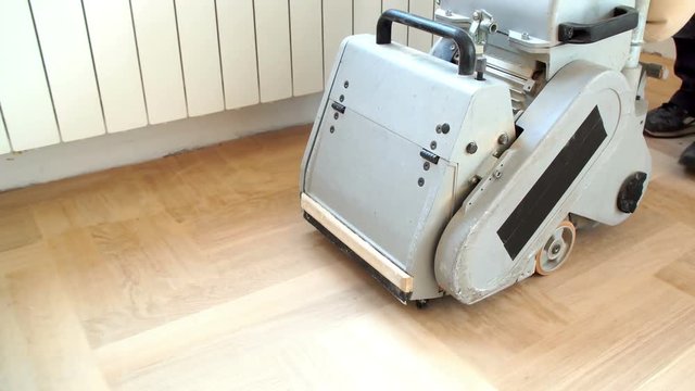 Sanding hardwood floor with the grinding machine. Repair in the apartment. Carpenter doing parquet wood floor polishing maintenance work by grinding machine