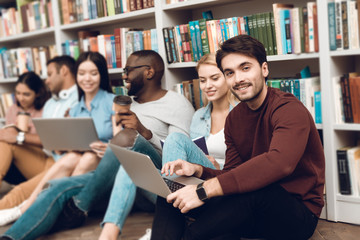 Group of ethnic multicultural students sitting near bookshelf in library.