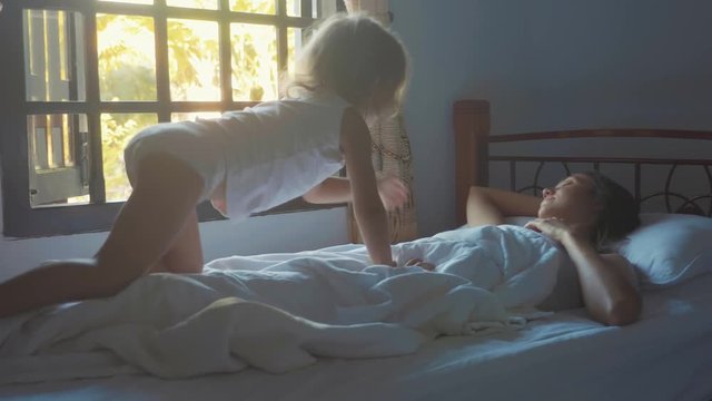 Cute little daughter wakes her mother at morning in slow motion.