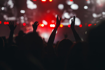 Crowd of people silhouettes with their hands up at music festival, rock concert. Dark red background, smoke, concert spotlights. 