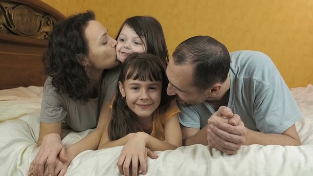 Family is playing in the bedroom. Portrait of a happy family. The parents with the children lie on the bed.