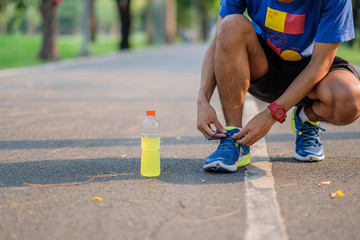 Young athlete man tying running shoes in the park outdoor, male runner ready for jogging on the road outside, asian Fitness walking and exercise on footpath in morning. wellness and sport concepts