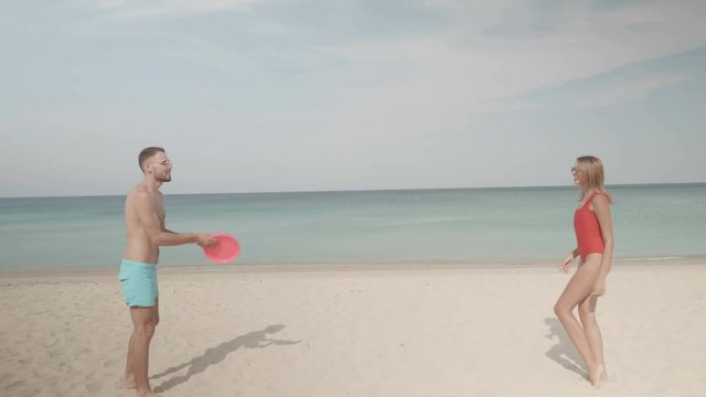Happy couple playing with frisbee flying disc on the beach during sunny summer day