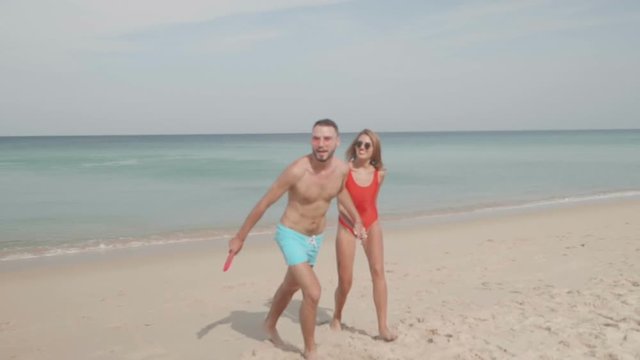 Happy couple playing with frisbee flying disc on the beach during sunny summer day - video in slow motion