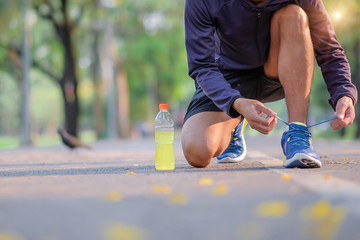 Young athlete man tying running shoes in the park outdoor, male runner ready for jogging on the road outside, asian Fitness walking and exercise on footpath in morning. wellness and sport concepts