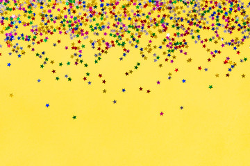 Scattered star shaped colorful glittering confetti over yellow background. Copy space.