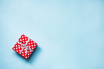 Obraz premium Top view of a red dotted gift box tied with silver bow over blue background. Copy space.