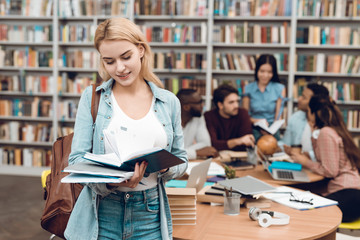 Group of ethnic multicultural students in library. White girl reading book.