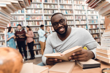 Ethnic african american guy surrounded by books in library. Student is reading book.