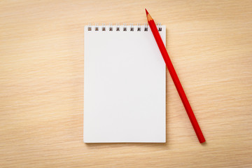 Red pencil with notebook on wooden table