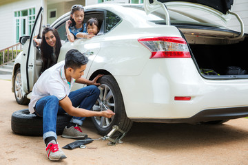 Father change a new tire but mother and daughter wait in car