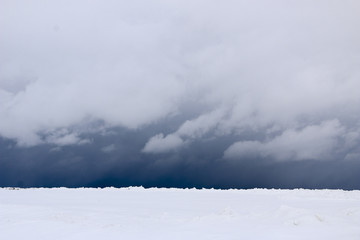 snow field. The plain is covered with white snow under a blue sky with thick white clouds. before a snowfall, a storm, a snowstorm. premonition of a blizzard. in anticipation of a blizzard.