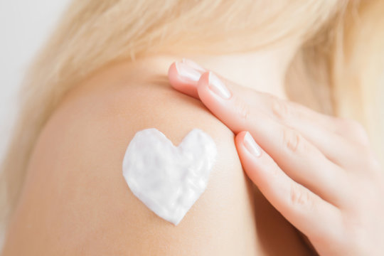 Groomed woman's hand applying moisturizing cream on her shoulder. Cares about clean and soft body skin. Heart shape created from cream. Love a body. Healthcare concept.