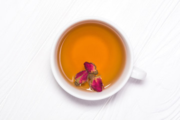 Natural tea from buds of a rose in a white cup on a white wooden background. View from above