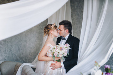 Kiss of the newlyweds. Enamored bride and groom. Gray interior.