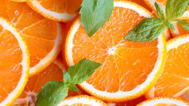 Slow pan of fresh bright oranges (orange fruits) slices decorated with mint leaves. Closeup.