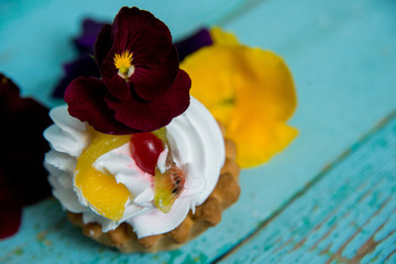 dessert: cake with cream and edible flowers (Pansy) on blue wooden background. the concept of vegetarianism and healthy eating