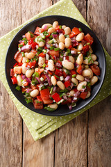 Homemade salad with beans, tomatoes, onions, peppers and herbs close-up on a plate. Vertical top view
