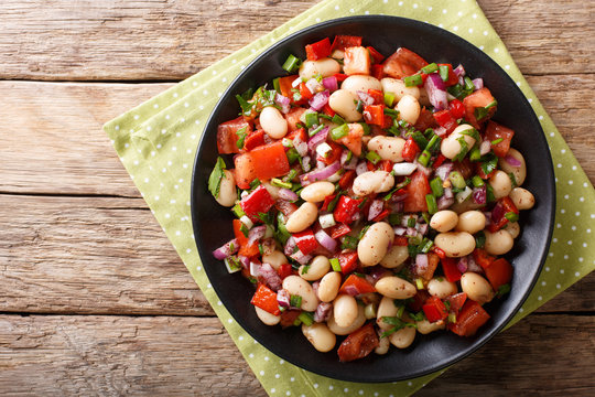 Homemade salad with beans, tomatoes, onions, peppers and herbs close-up on a plate. horizontal top view