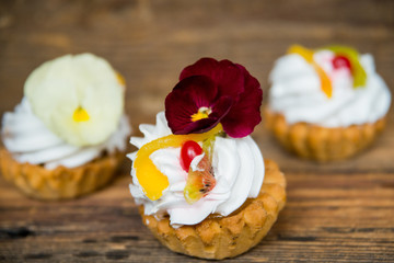 Obraz na płótnie Canvas dessert: cake with cream and edible flowers (Pansy) on natural wooden background. the concept of natural nutrition, the use of colors in cooking